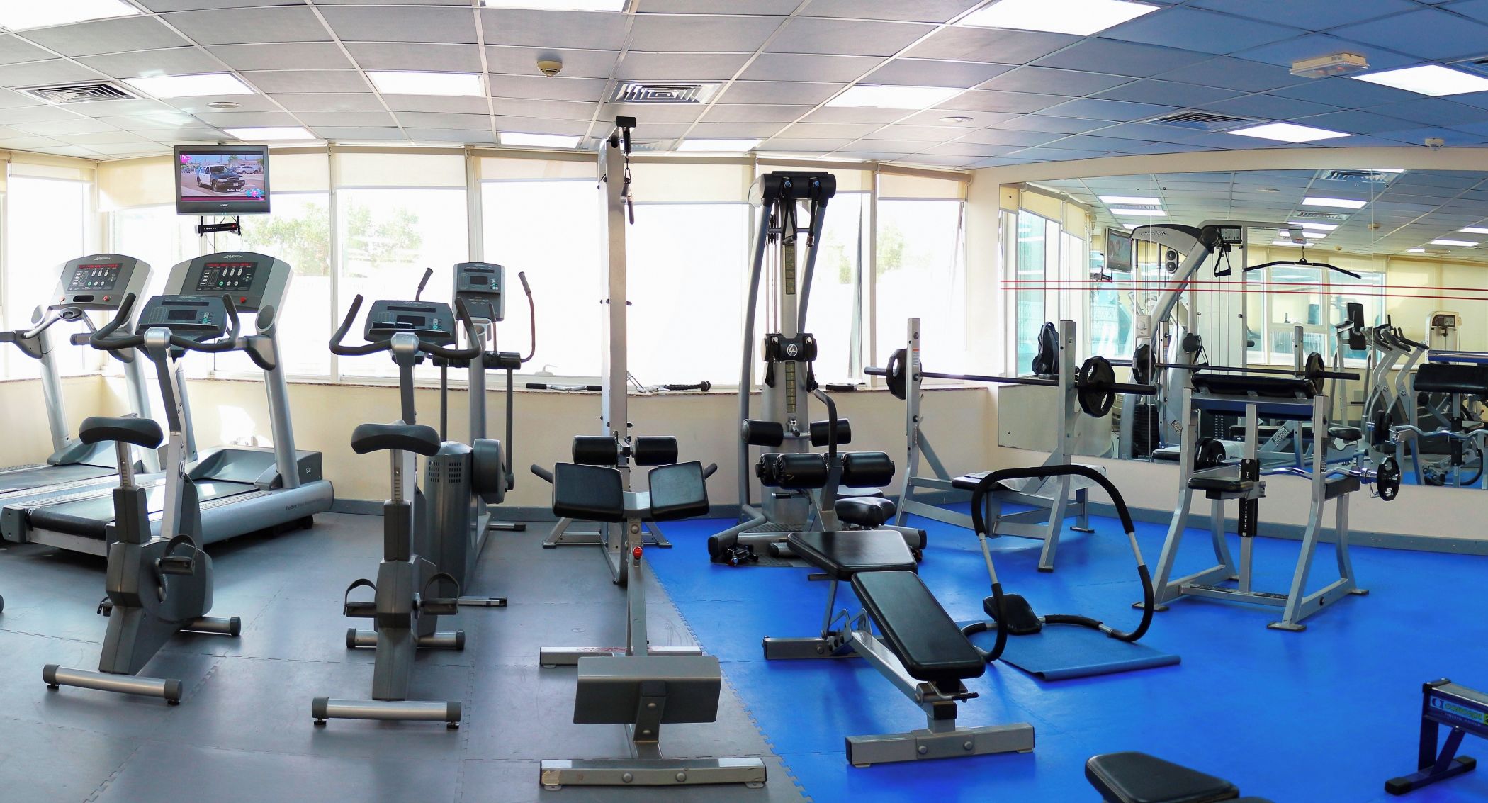 Une salle de sport équipée de tapis de course, d’appareils de musculation et d’un mur recouvert de miroirs.