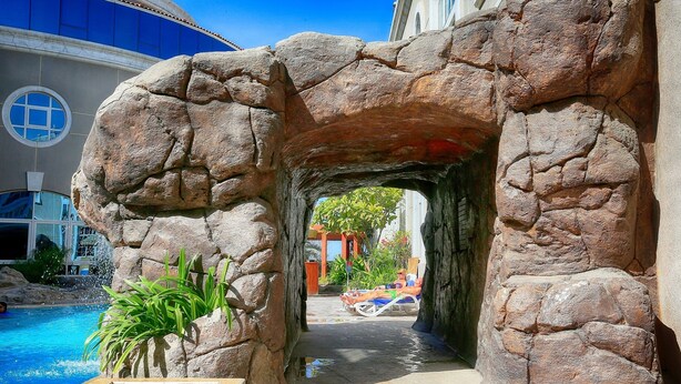 Uma área de piscina com um arco de pedra natural, a piscina e um espaço de descanso com vista para a piscina.