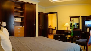 Ein Hotelzimmer mit einem großen Bett, einem Kleiderschrank, einem Schreibtisch mit Stuhl, einem Fernseher und einem kleinen Tisch mit Blumen.