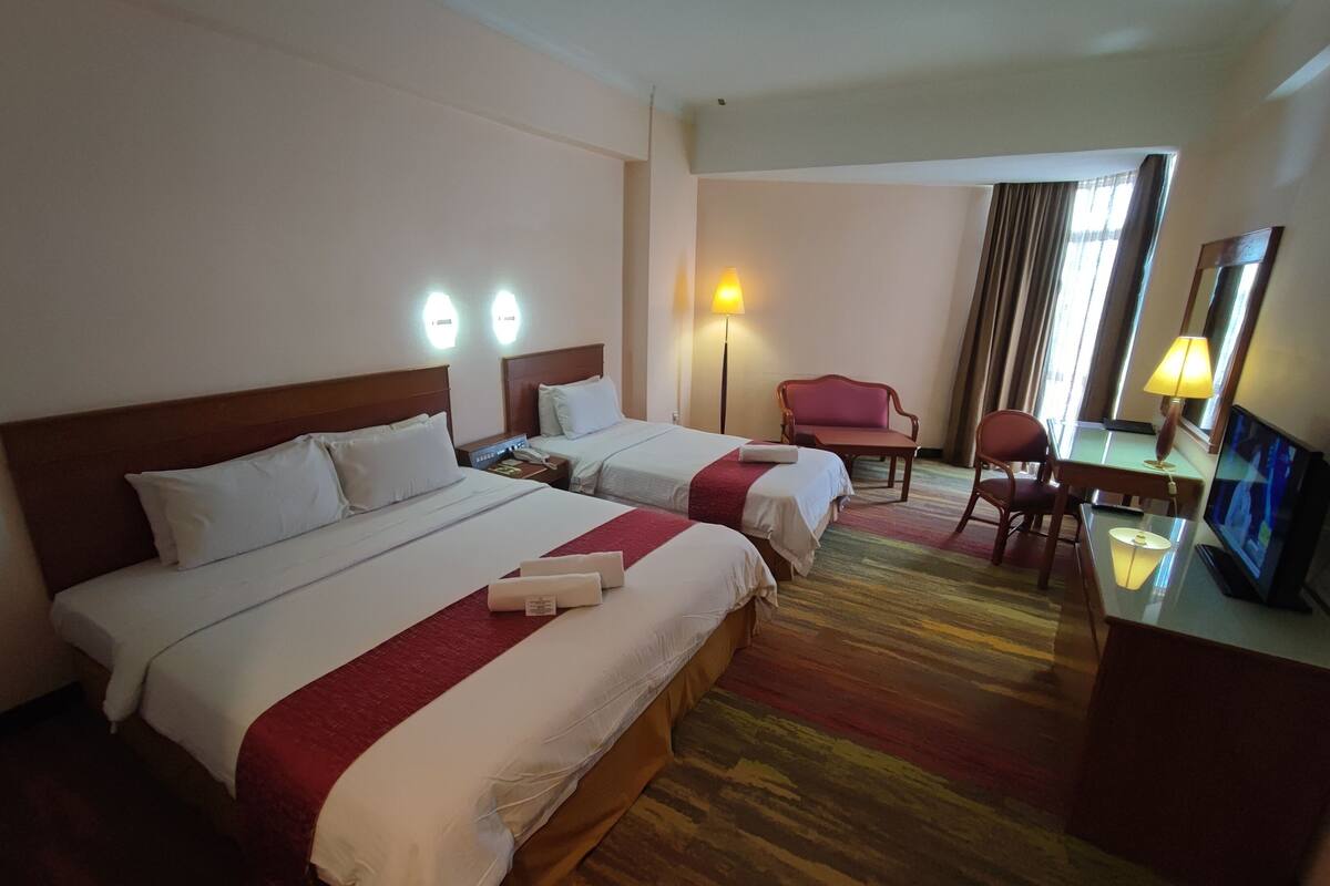 A hotel room with two beds, a desk, a chair, a TV, and a lamp.