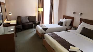 A hotel room with two beds, a sofa, a desk with a lamp, a telephone, and a TV.
