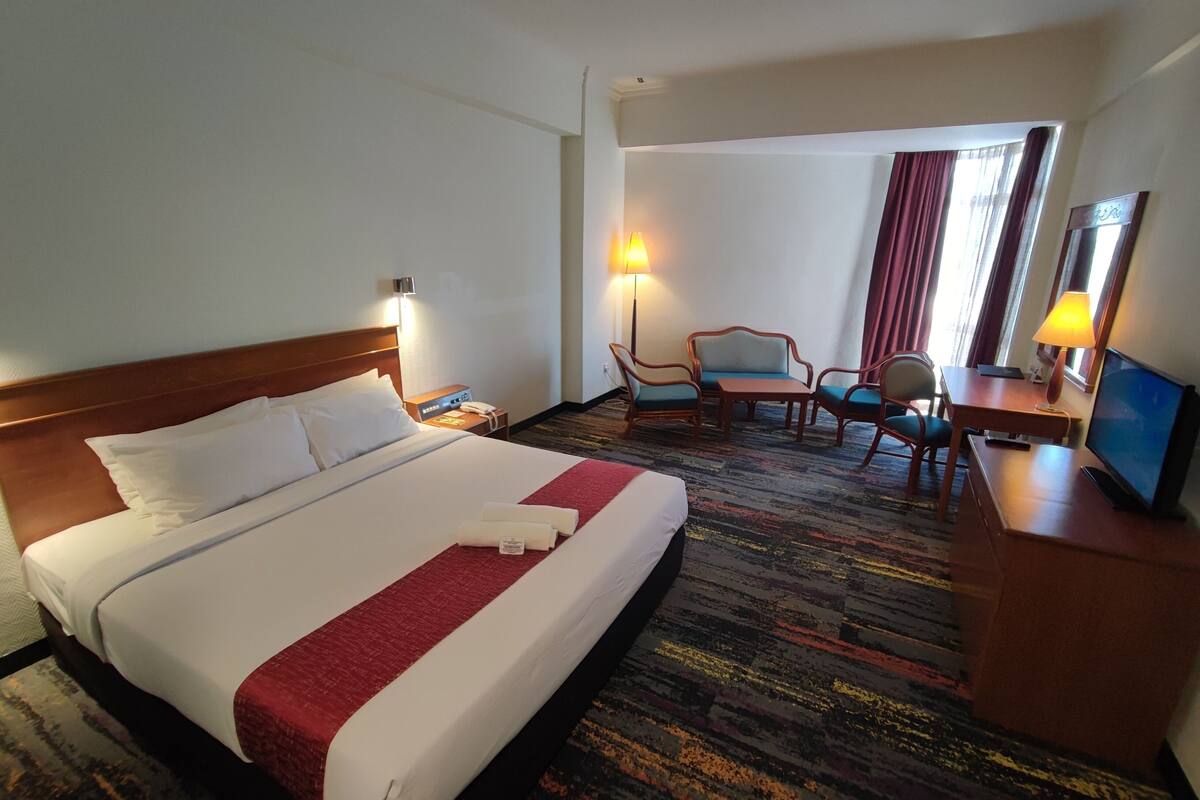 A hotel room with a large bed, a desk with a chair, a TV, and a lamp.