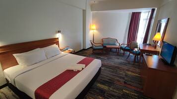 Een hotelkamer met een groot bed, een bureau met stoel, een televisie en een lamp.