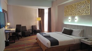 Hotellihuone, jossa on sänky, työpöytä, tuoleja ja televisio.