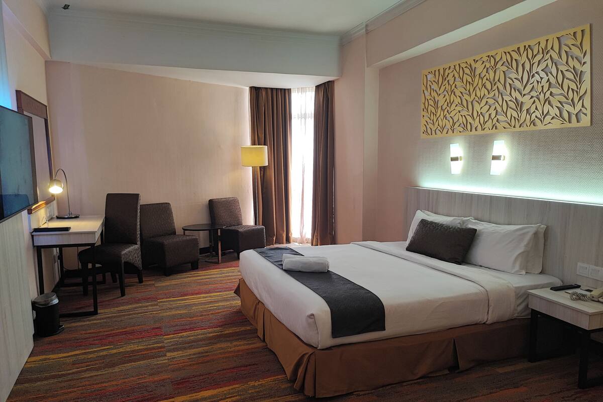 A hotel room with a bed, desk, chairs, and a TV.