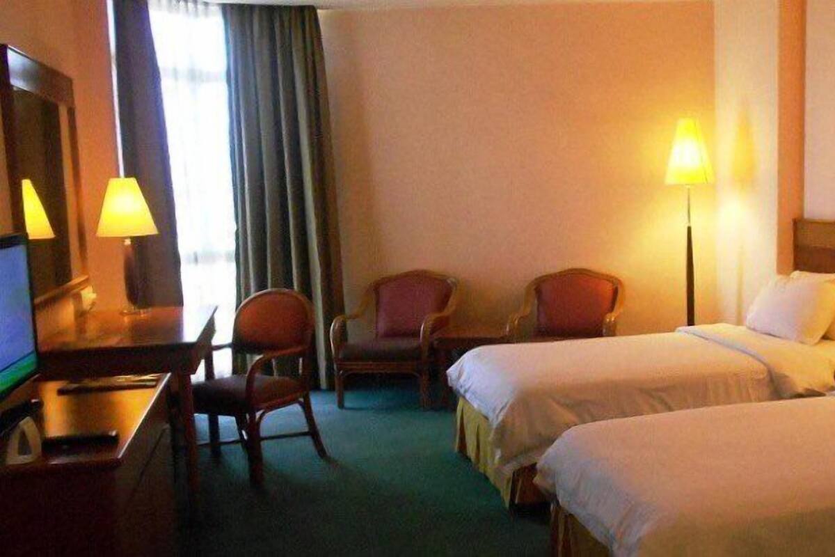 A hotel room with two beds, a desk with a computer, two chairs, and lamps.