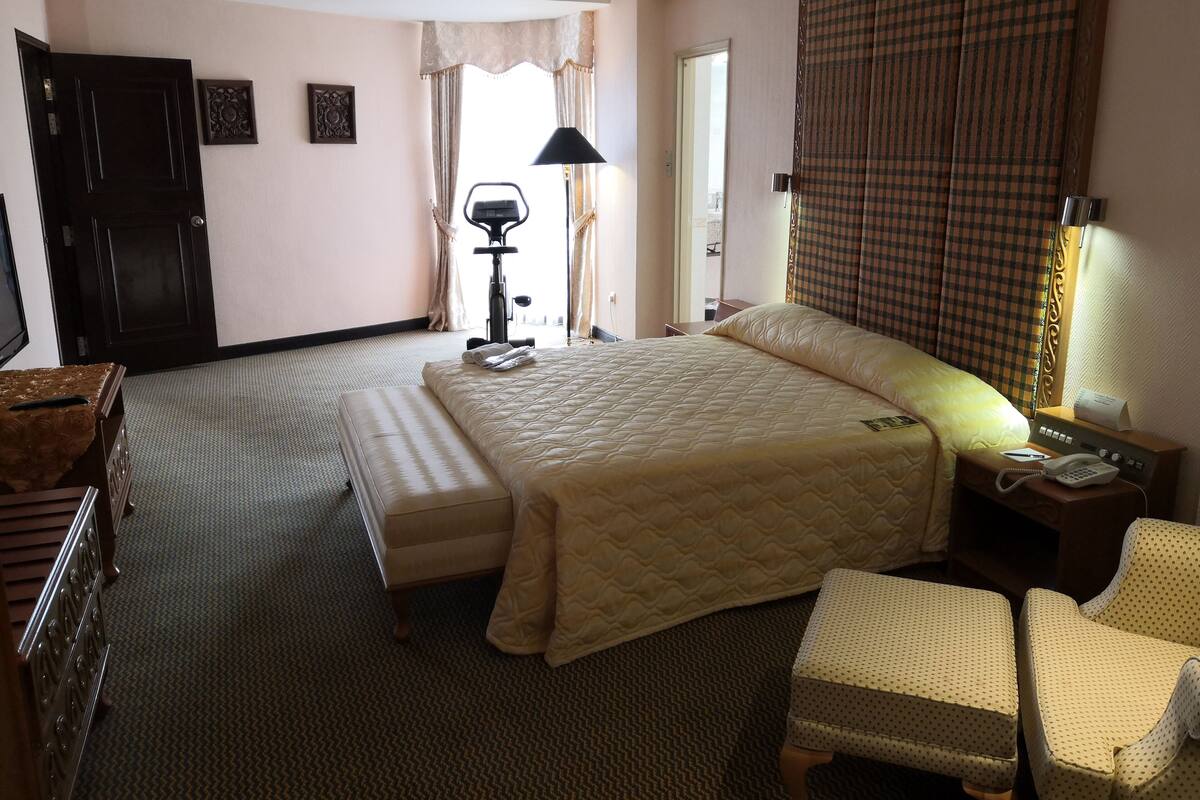 A hotel room with a large bed, a desk, a chair, a desk lamp, and a telephone.