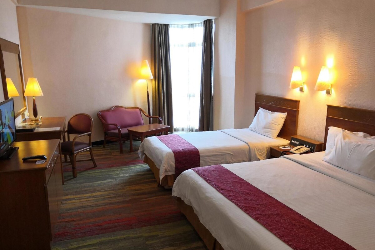 A hotel room with two beds, a desk with a chair, a television, and lamps.