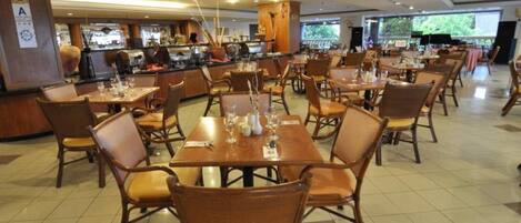 A spacious dining area with multiple tables and chairs, a central counter, and a view of the outdoors through large windows.