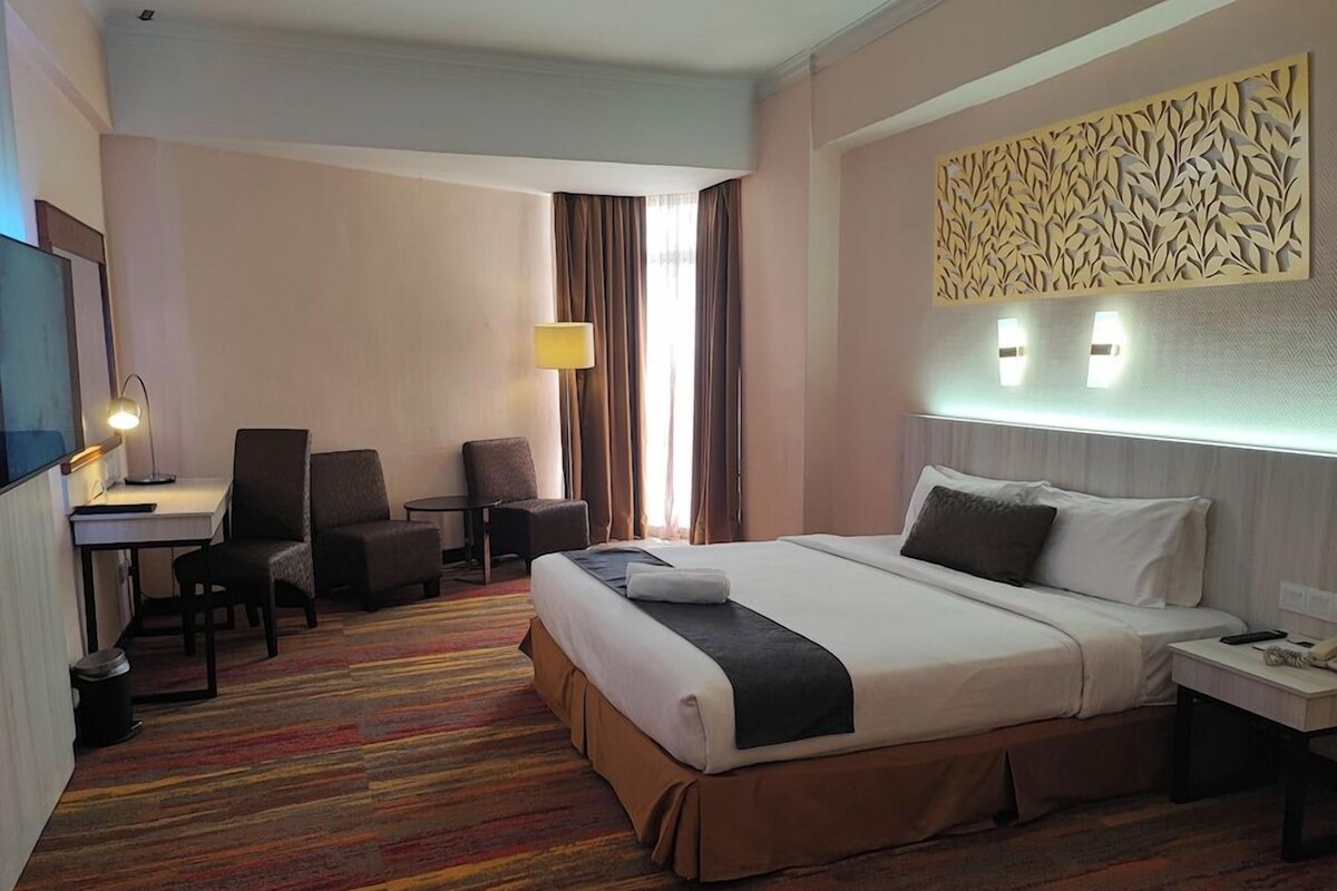 A hotel room with a large bed, a desk, a chair, and a TV.