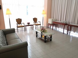 Una sala moderna con un sofá, dos sillones, una mesa de centro de vidrio con un centro de flores, una mesita con una lámpara y un escritorio con una silla.