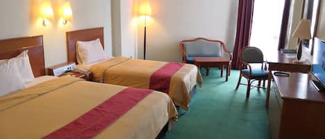 Habitación de hotel con dos camas, un escritorio, una silla, un televisor y una lámpara.