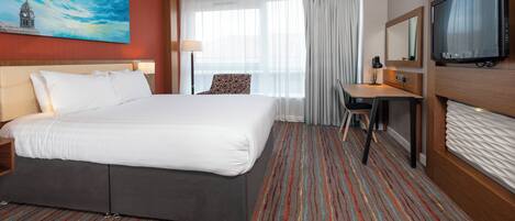 Habitación de hotel con una cama grande, escritorio, televisor y ventana con cortinas.