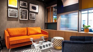 A modern living room with a sofa, ottomans, and a glass coffee table. - Holiday Inn Derby Riverlights by IHG (Derby)