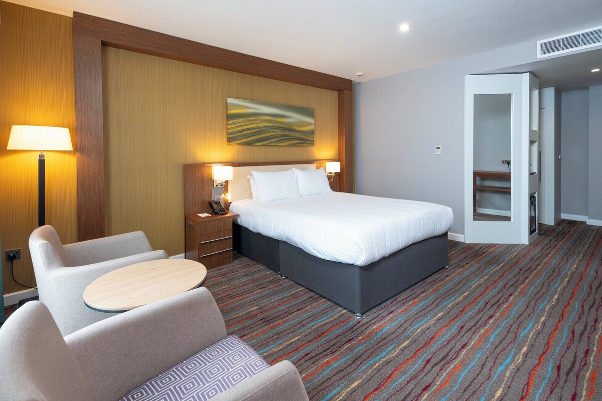 A hotel room with a bed, bedside lamps, a desk, a chair, and a carpeted floor.