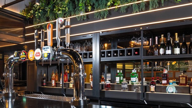A bar area with multiple taps, shelves of liquor bottles, and a green plant decoration. - Holiday Inn Derby Riverlights by IHG (Derby)