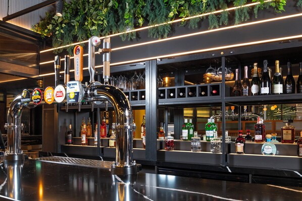 A bar area with multiple taps, shelves of liquor bottles, and a green plant decoration. - Holiday Inn Derby Riverlights by IHG (Derby)