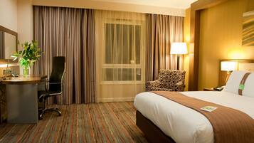 Une chambre d’hôtel avec un grand lit, un bureau avec une chaise, une chaise à motifs léopard, une lampe et une fenêtre avec des rideaux.