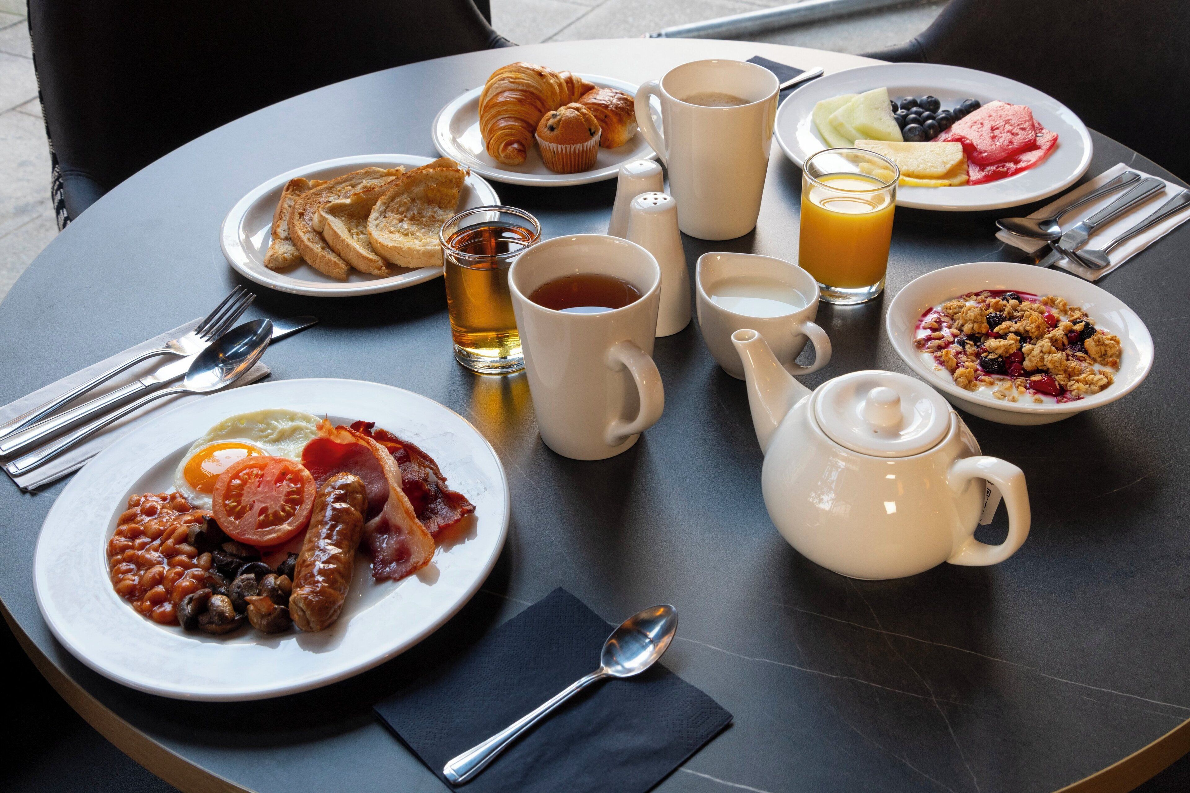 A breakfast table with plates of toast, croissants, eggs, and various fruits and beverages.