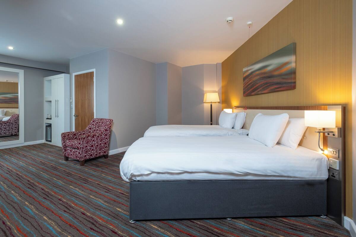 Una habitación de hotel con una cama grande, una silla y un cuadro en la pared.