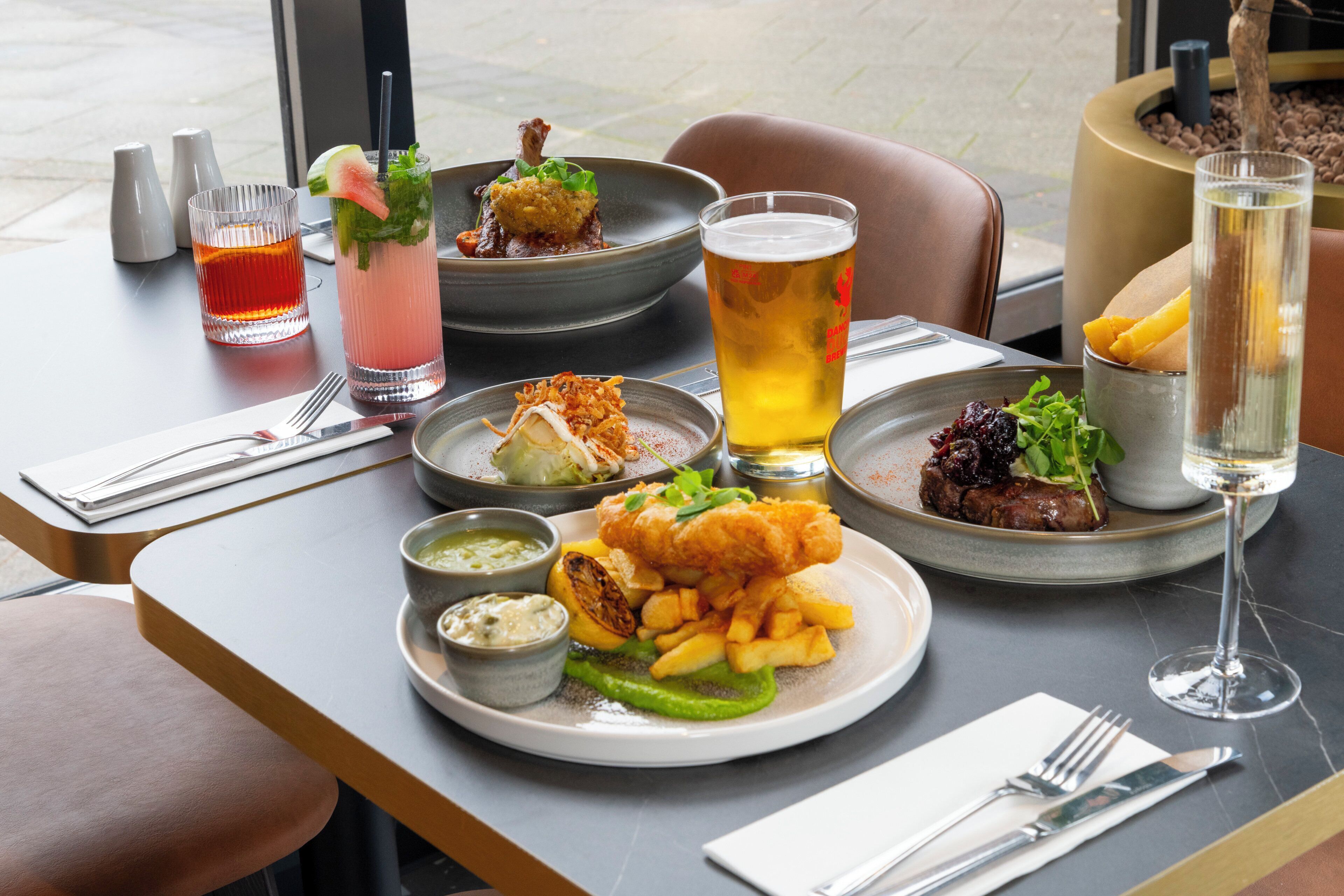 A dining table with various dishes, drinks, and a potted plant.