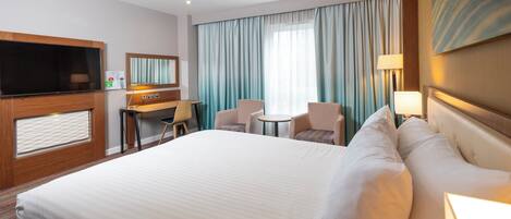 A hotel room with a large bed, a desk with a chair, a television, and a window with curtains.