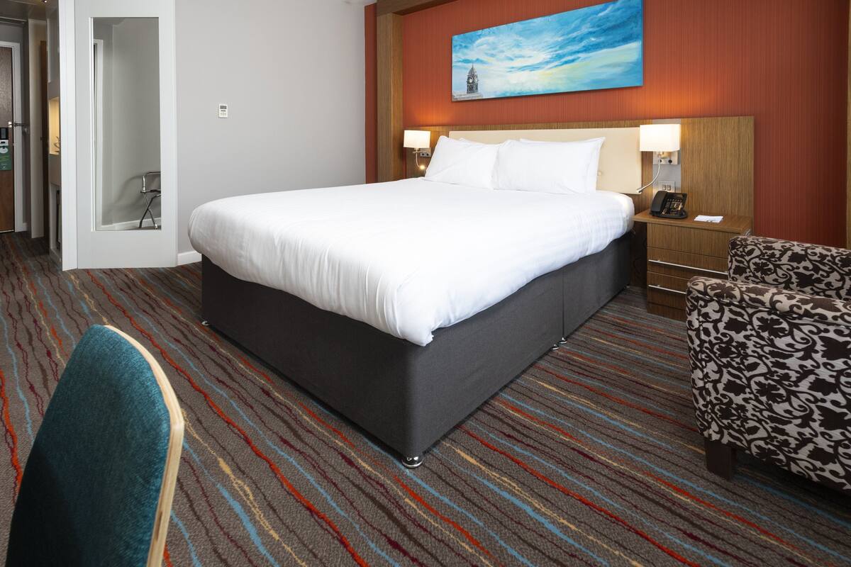 Habitación de hotel con una cama grande, un escritorio con teléfono, una silla y un cuadro en la pared.