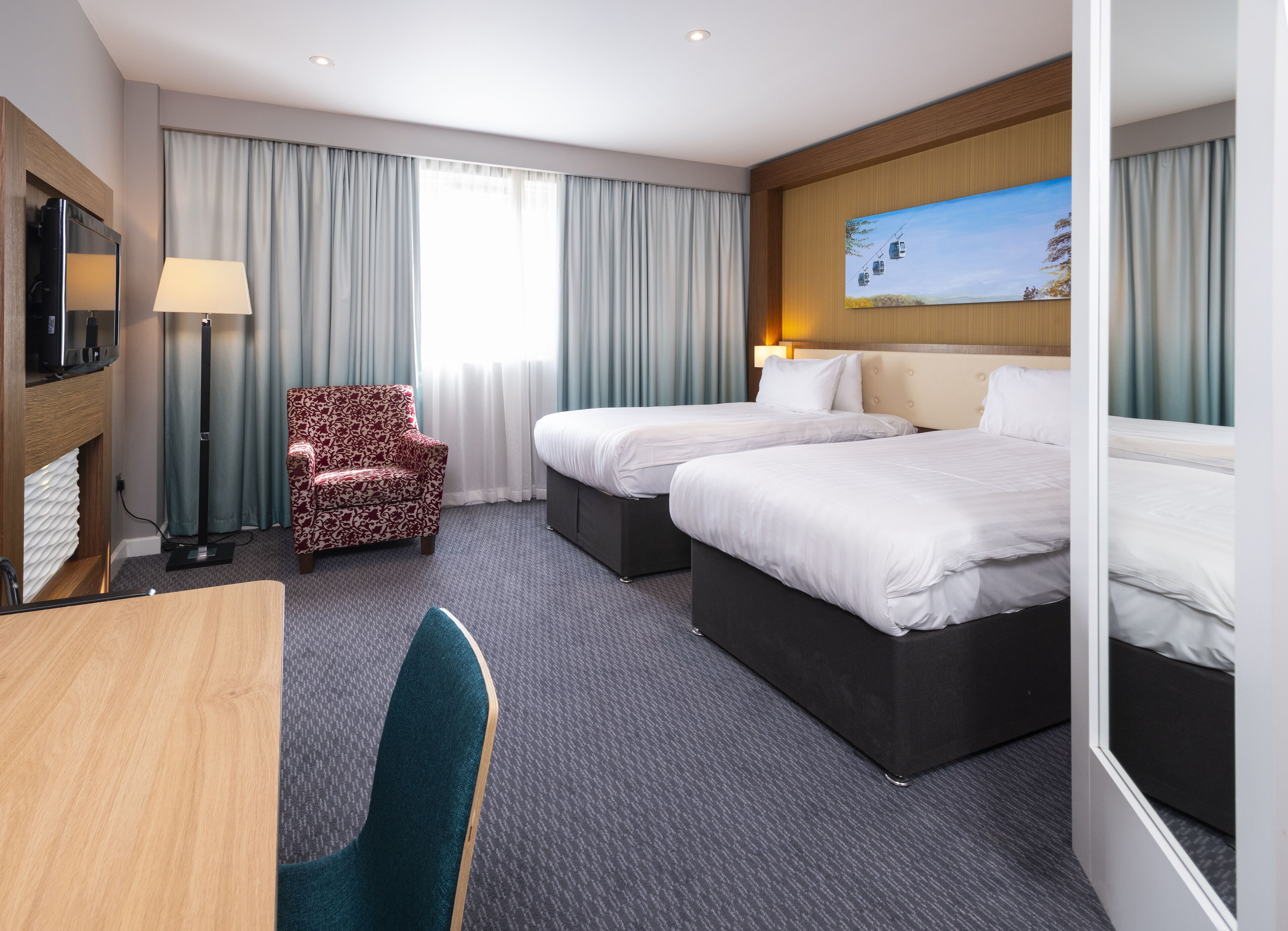 Habitación de hotel con dos camas, un escritorio, una silla, un televisor y un cuadro en la pared.