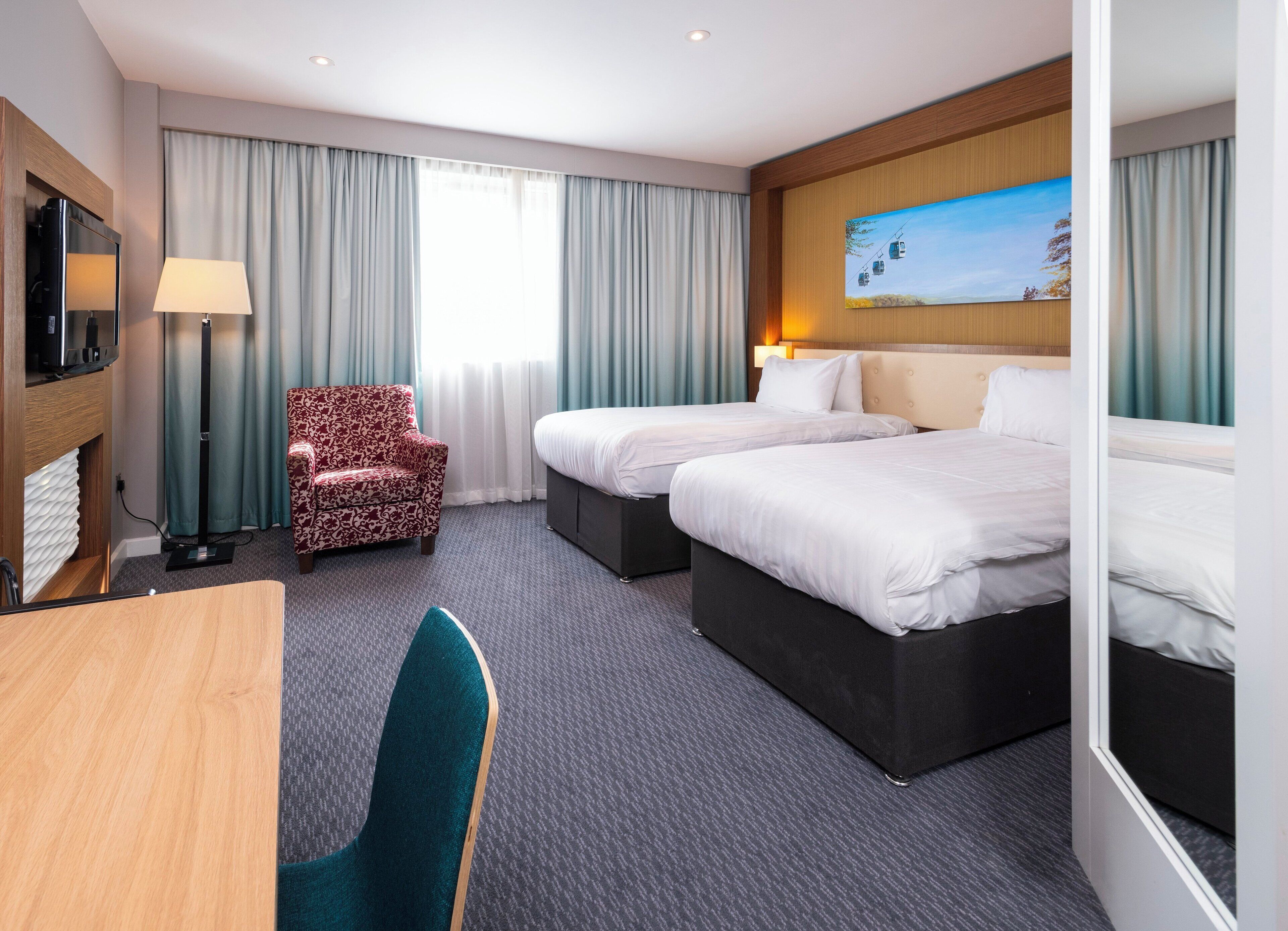 A hotel room with two beds, a desk, a chair, a TV, and a painting on the wall.