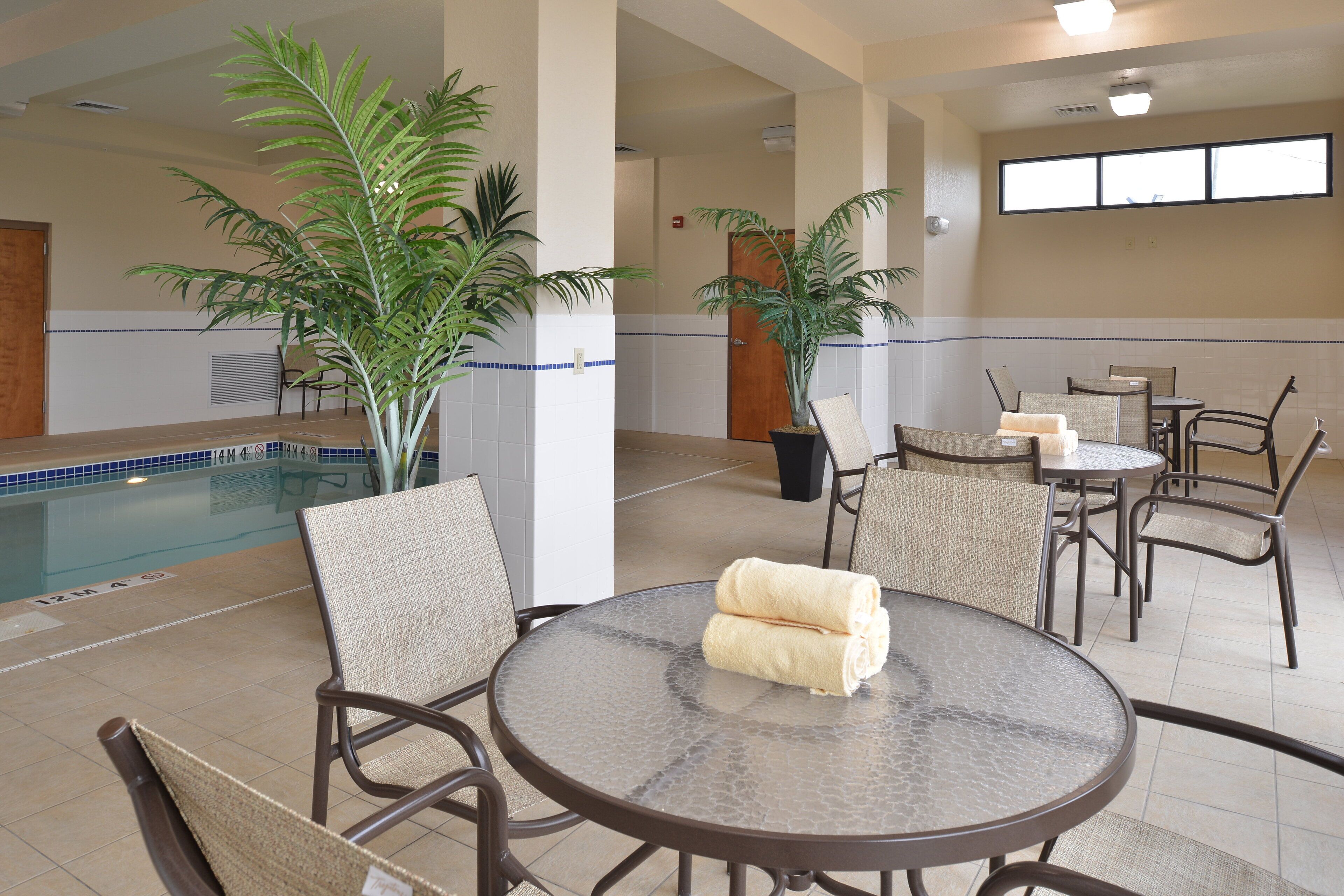 A pool area with lounge chairs and a table, surrounded by potted plants.
