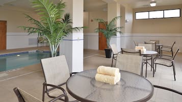 A pool area with lounge chairs and a table, surrounded by potted plants.