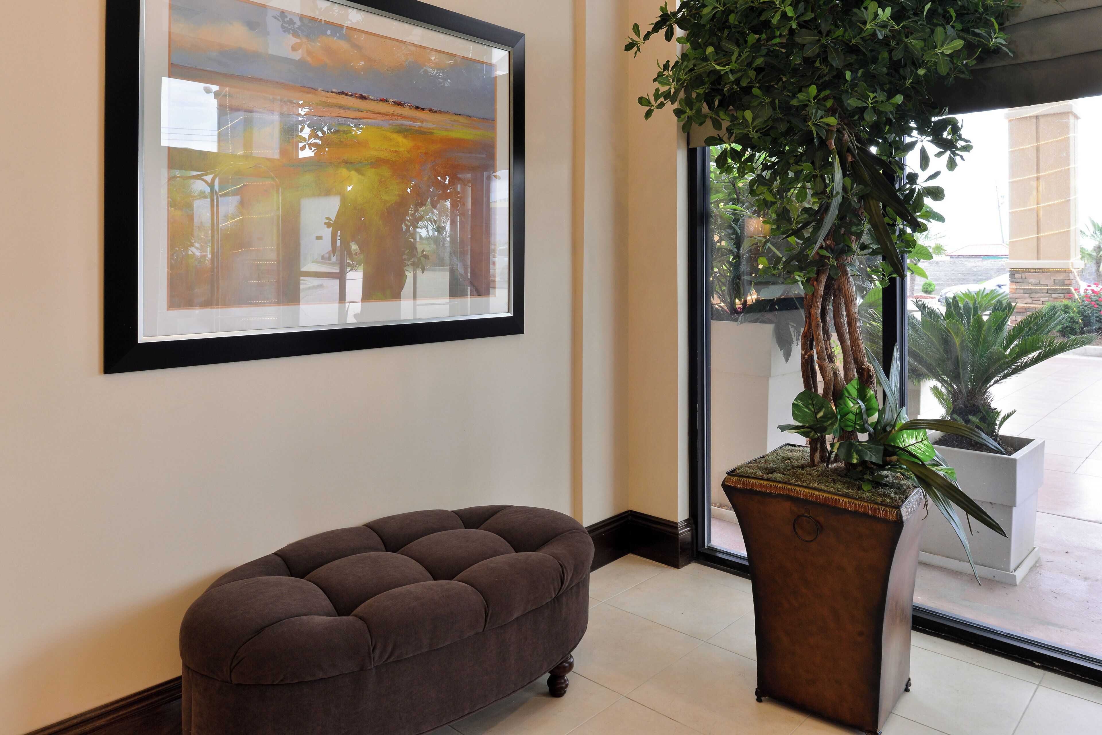 Une pièce décorée avec un tableau abstrait encadré, un pouf capitonné et une plante en pot.