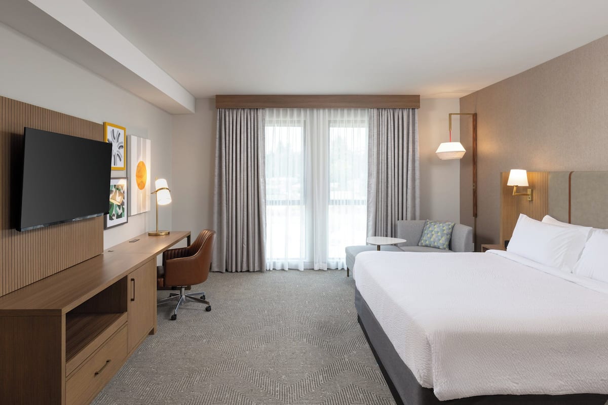 Habitación de hotel con una cama grande, un escritorio con silla, televisor montado en la pared y ventana con cortinas.