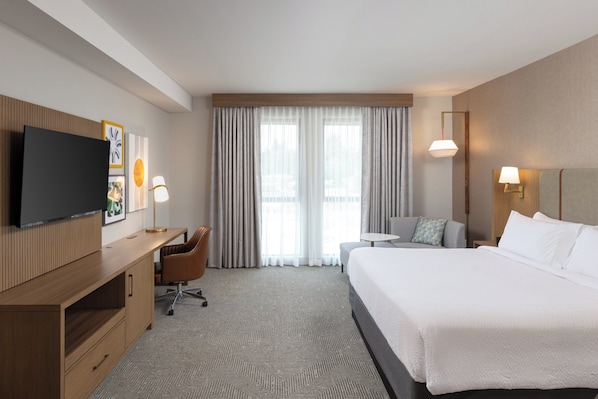 A hotel room with a large bed, a desk with a chair, a TV mounted on the wall, and a window with curtains. - Holiday Inn Montgomery Airport South by IHG (Montgomery)