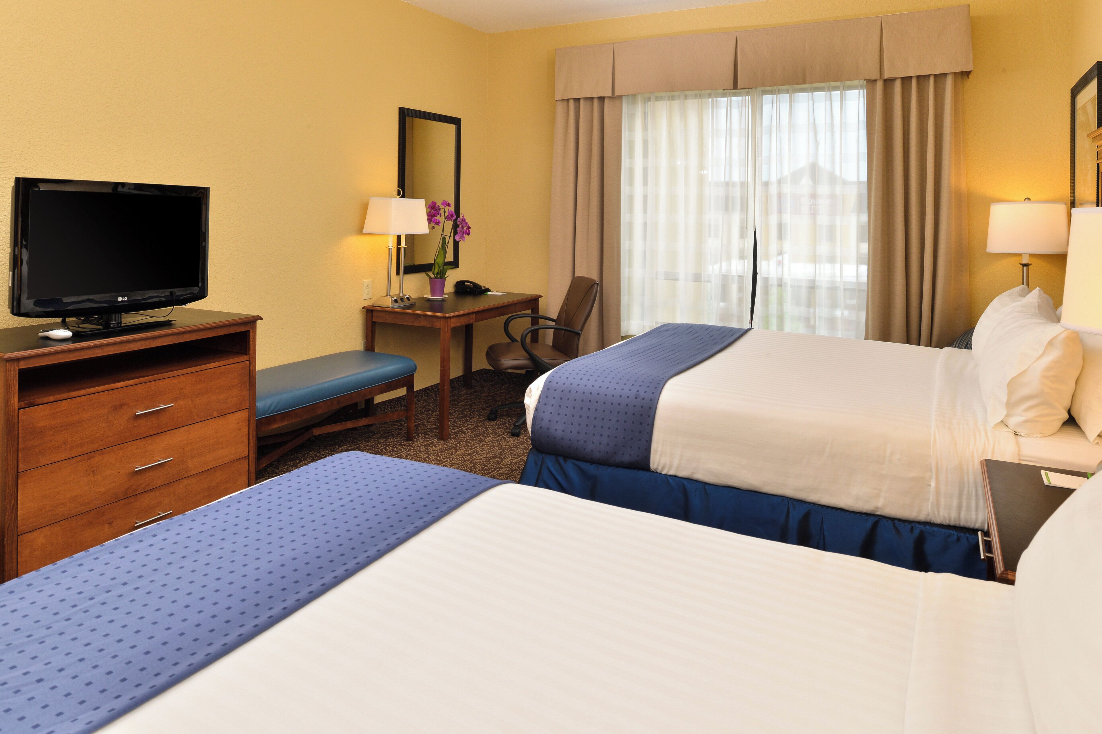 A hotel room with a bed, a desk with a computer, a television, and a chair.