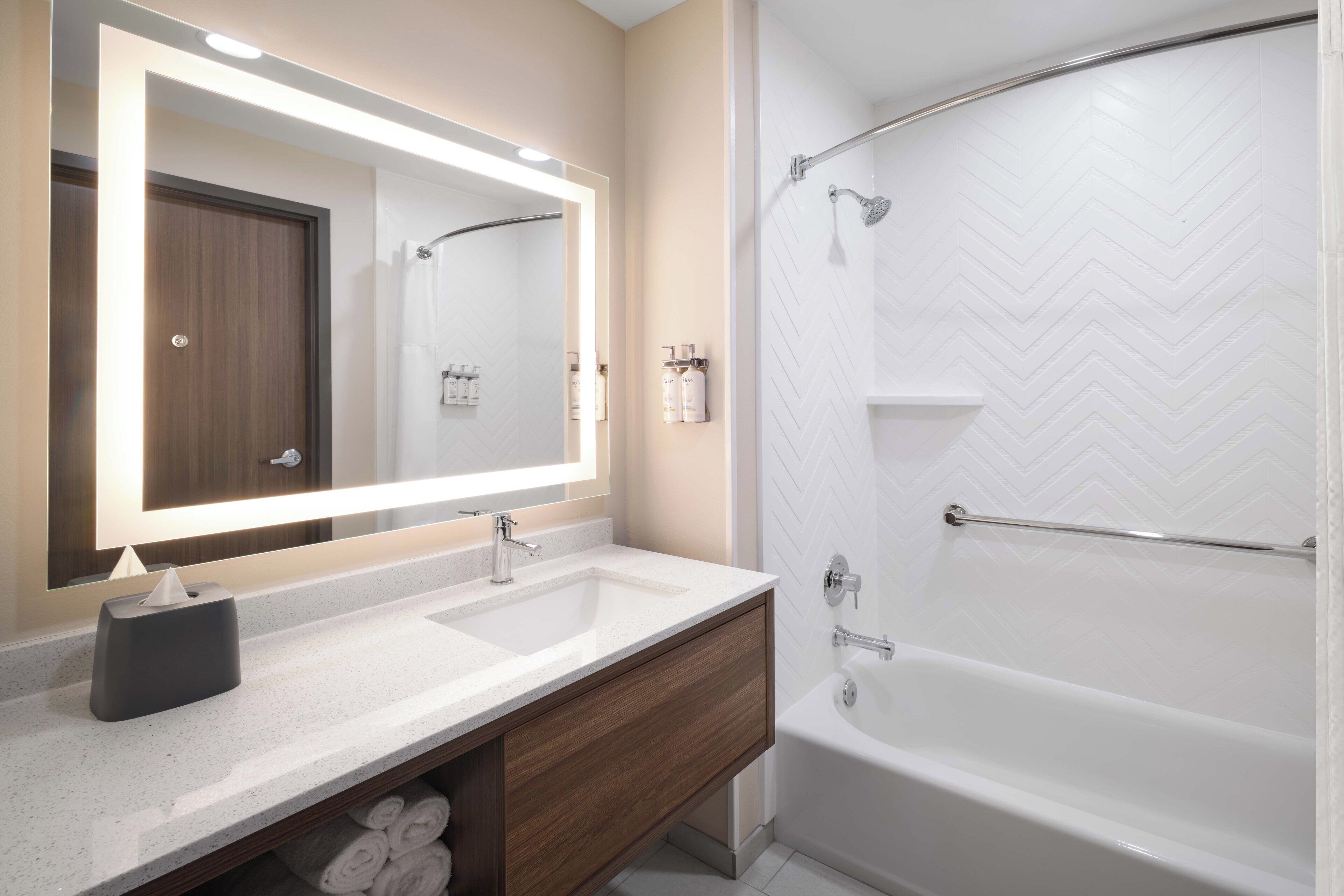 Un baño moderno con dos lavamanos, un espejo grande, una ducha con un patrón de baldosas blancas tipo espiga y un perchero para toallas.