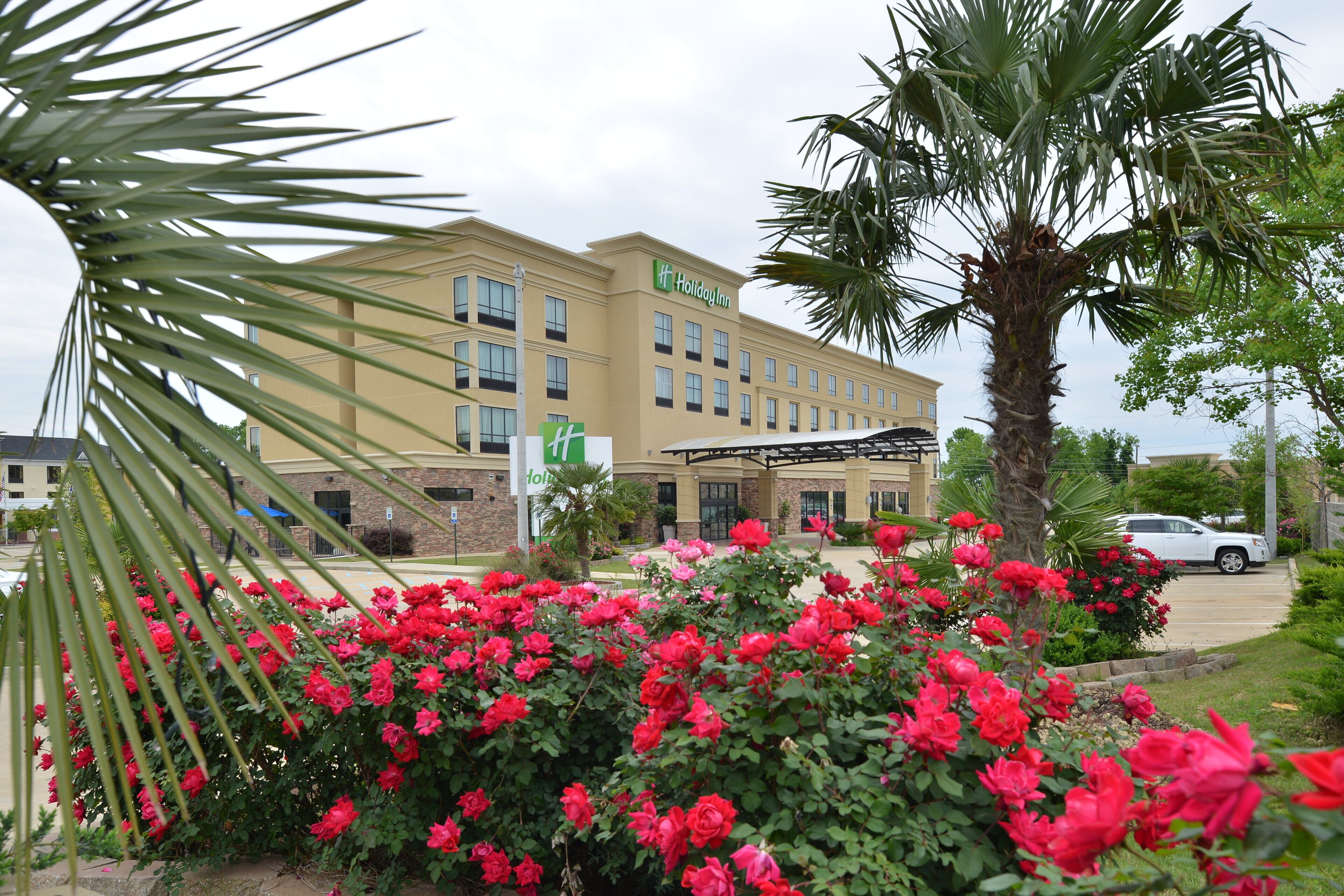 A Holiday Inn hotel with a covered outdoor area, palm trees, and red flowers.