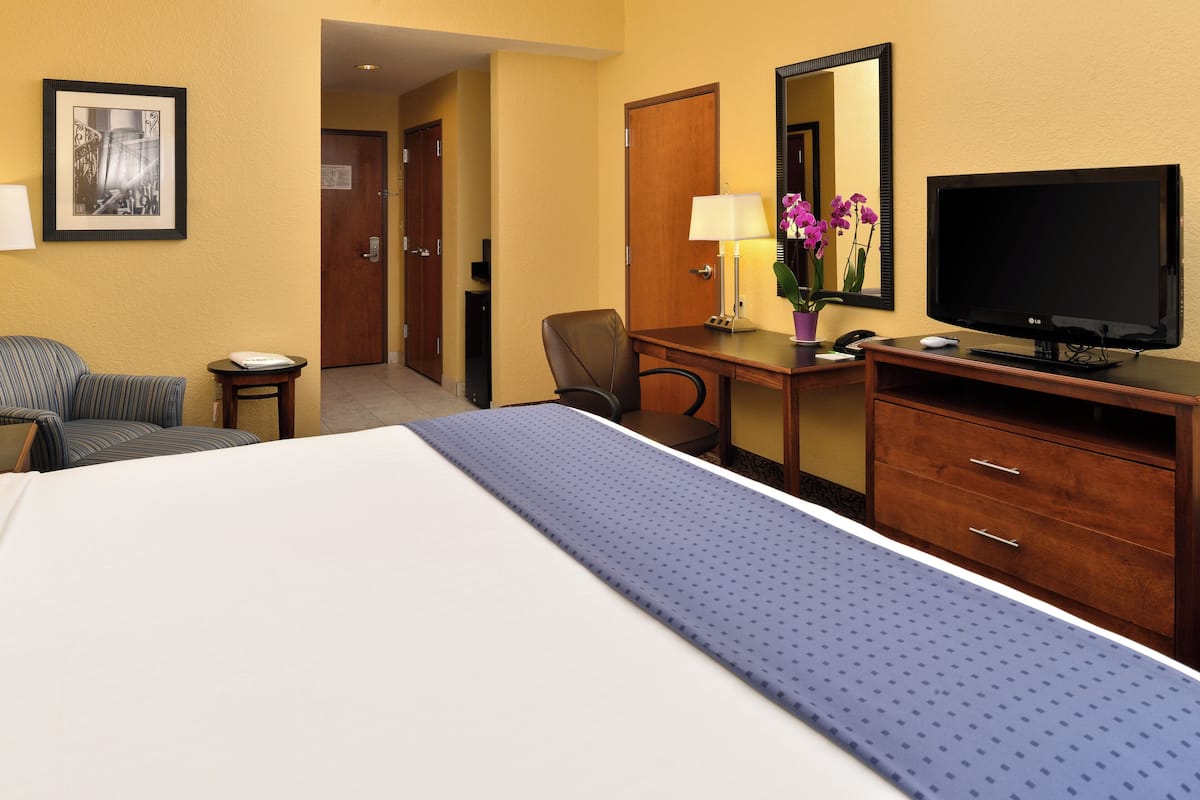 Una habitación de hotel con cama, escritorio con computadora, televisión y silla.
