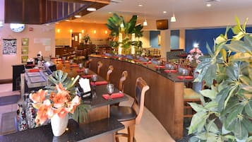 Un restaurant doté d’un comptoir incurvé, de plusieurs tables, de chaises et d’une variété de plantes.