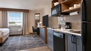A compact hotel room with a kitchenette, a bed, a desk, and a window with curtains. - Candlewood Suites Fayetteville Fort Bragg by IHG (Fayetteville)