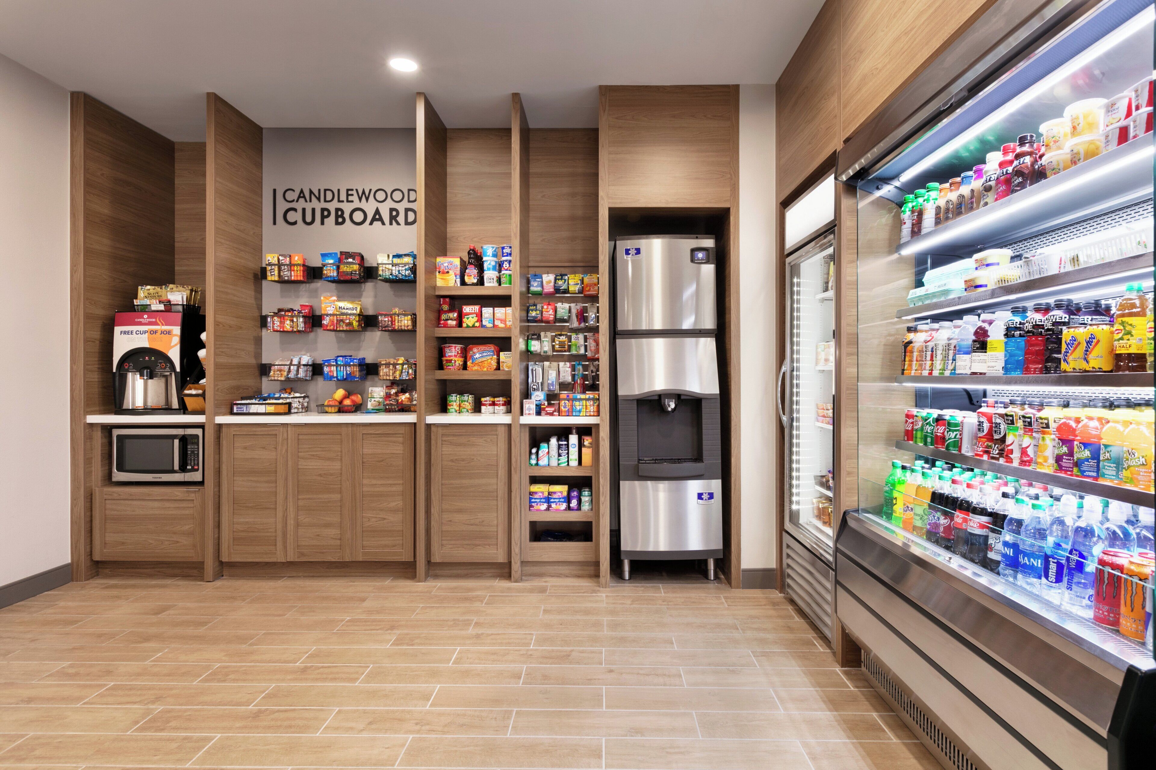 Una estación de autoservicio con bebidas y aperitivos variados, un microondas y un refrigerador.