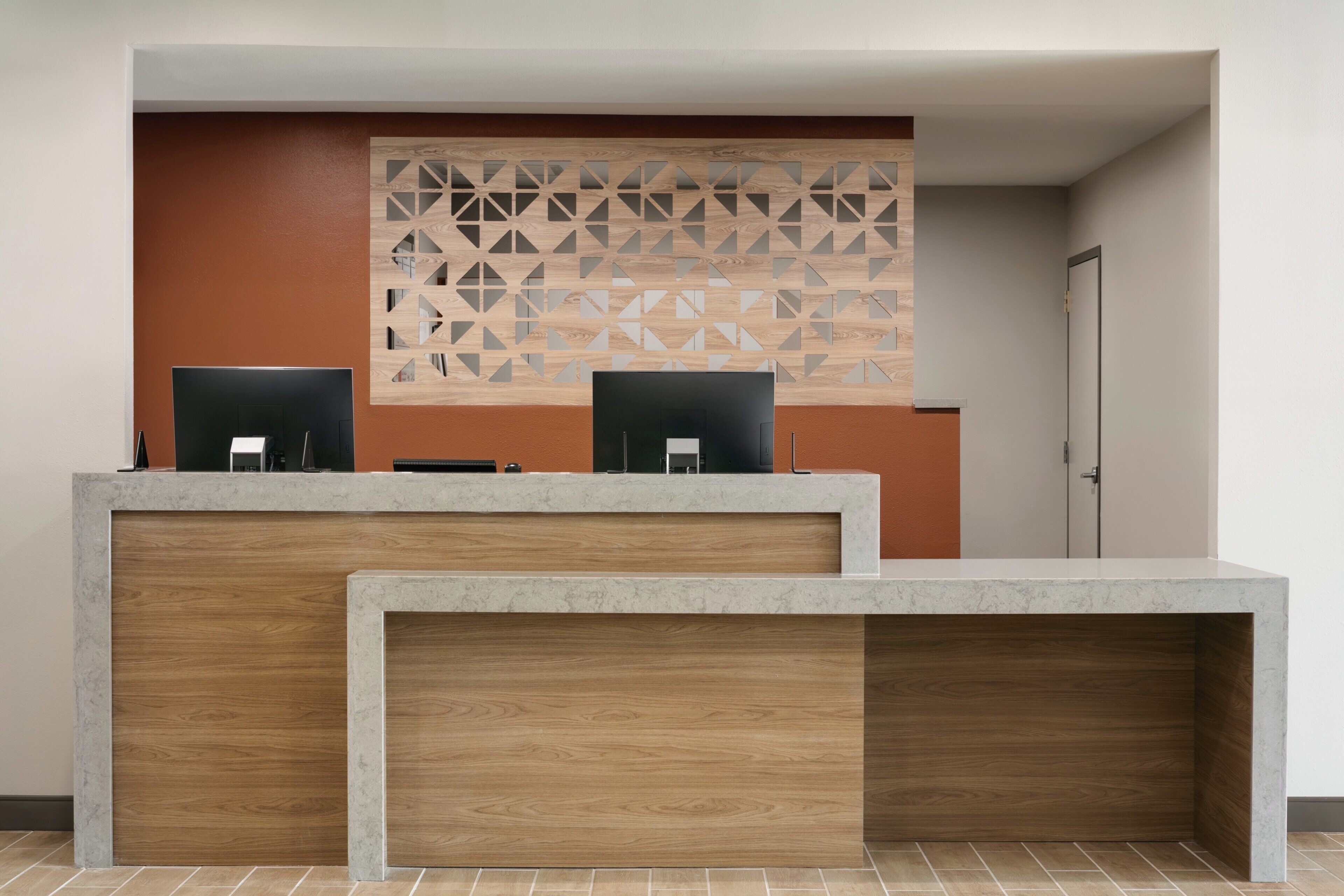 A reception desk with two computer monitors, a wooden panel wall, and a door to the right.