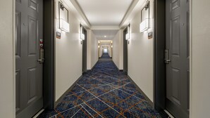 A hotel hallway with carpeted floors, doors on both sides, and wall-mounted light fixtures. - Candlewood Suites Fayetteville Fort Bragg by IHG (Fayetteville)