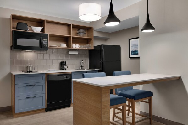 A modern kitchen with a built-in microwave, coffee maker, and a black refrigerator.
