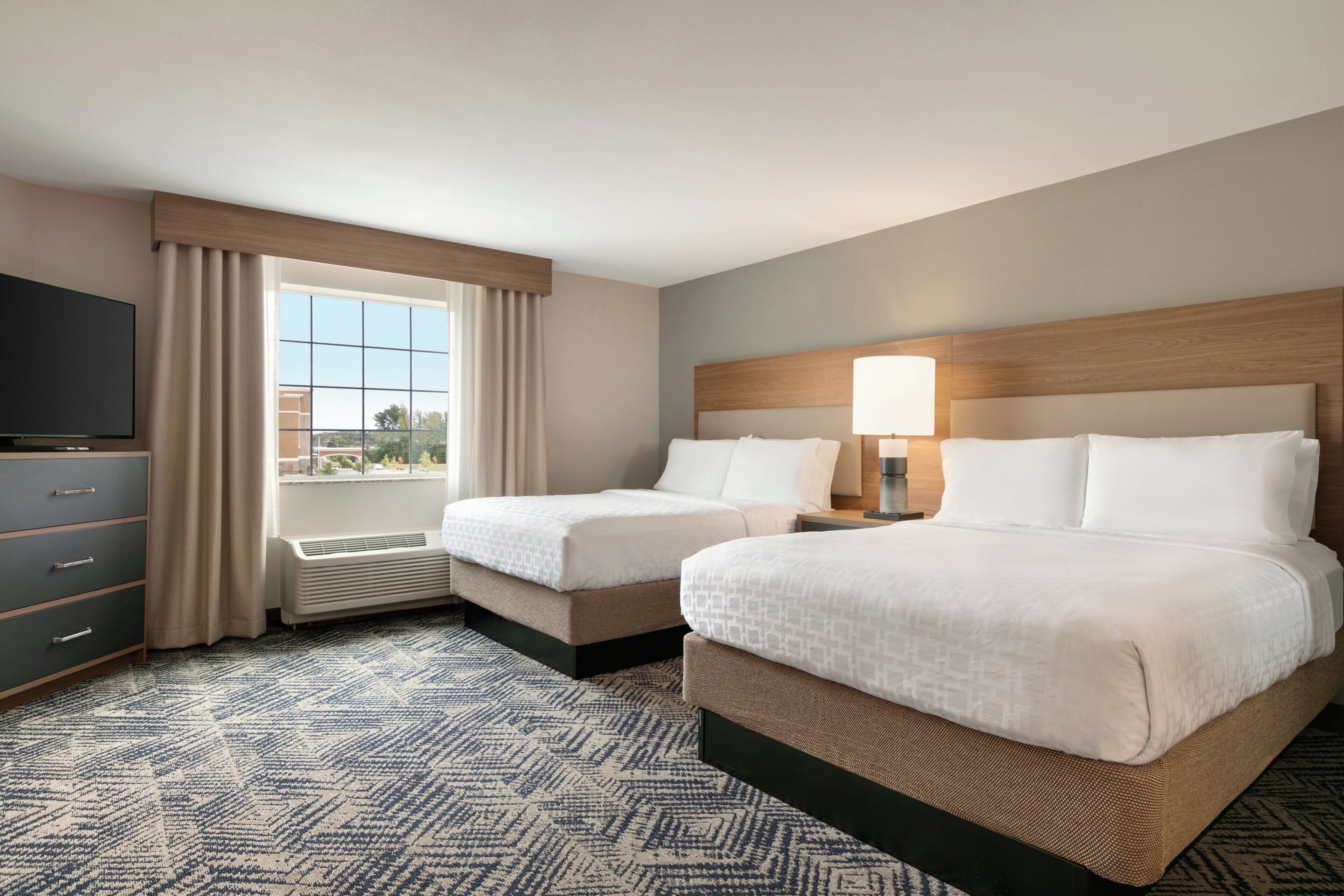 A hotel room with two beds, a TV, a window with curtains, and a patterned carpet.