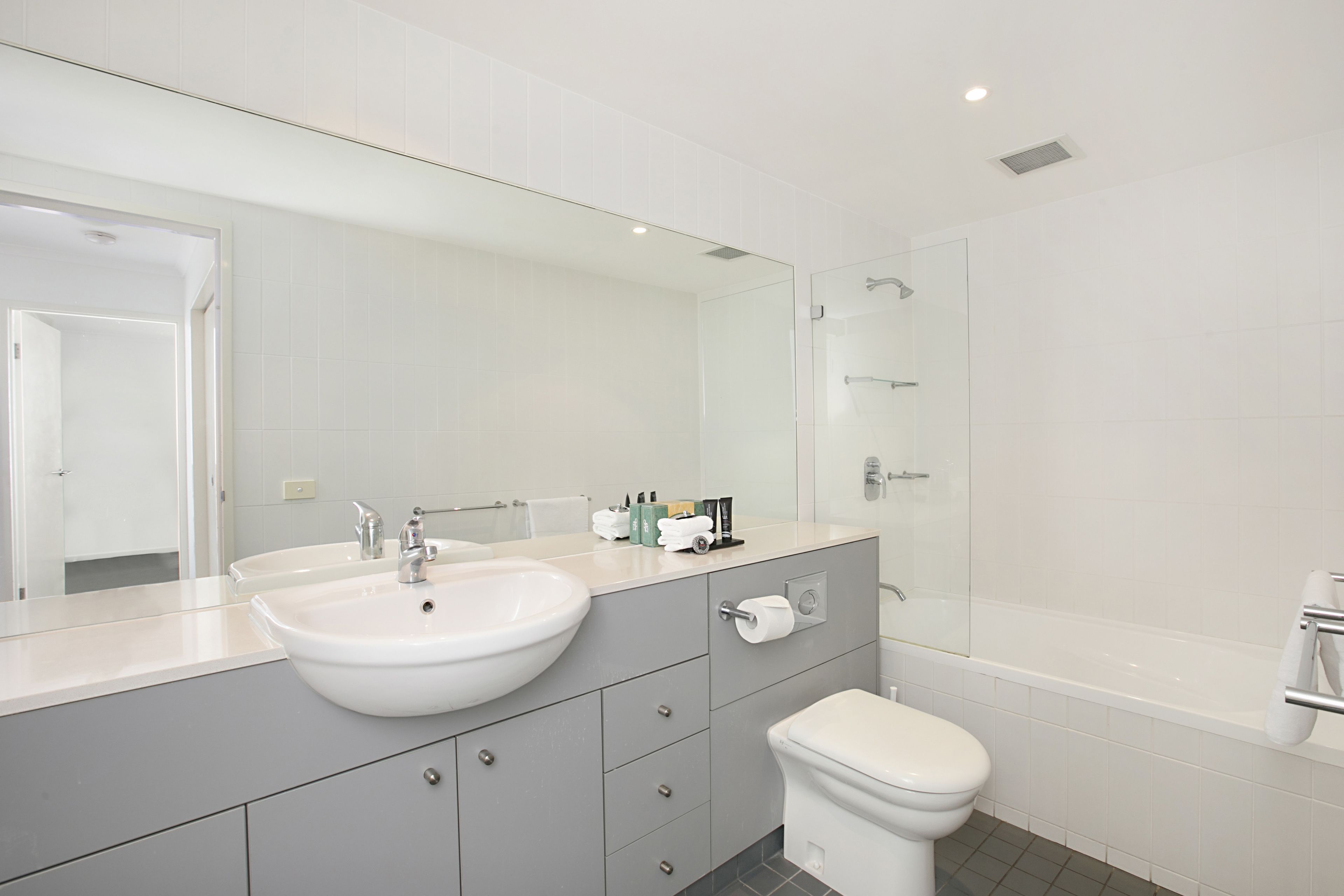 A modern bathroom with a large mirror, a sink, a toilet, and a shower area.