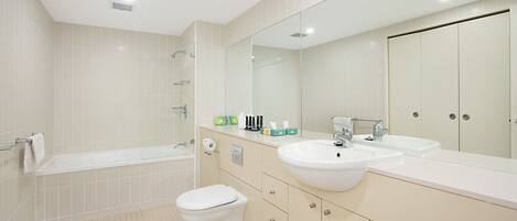 Un baño moderno con bañera, inodoro y tocador con lavamanos y espejo.