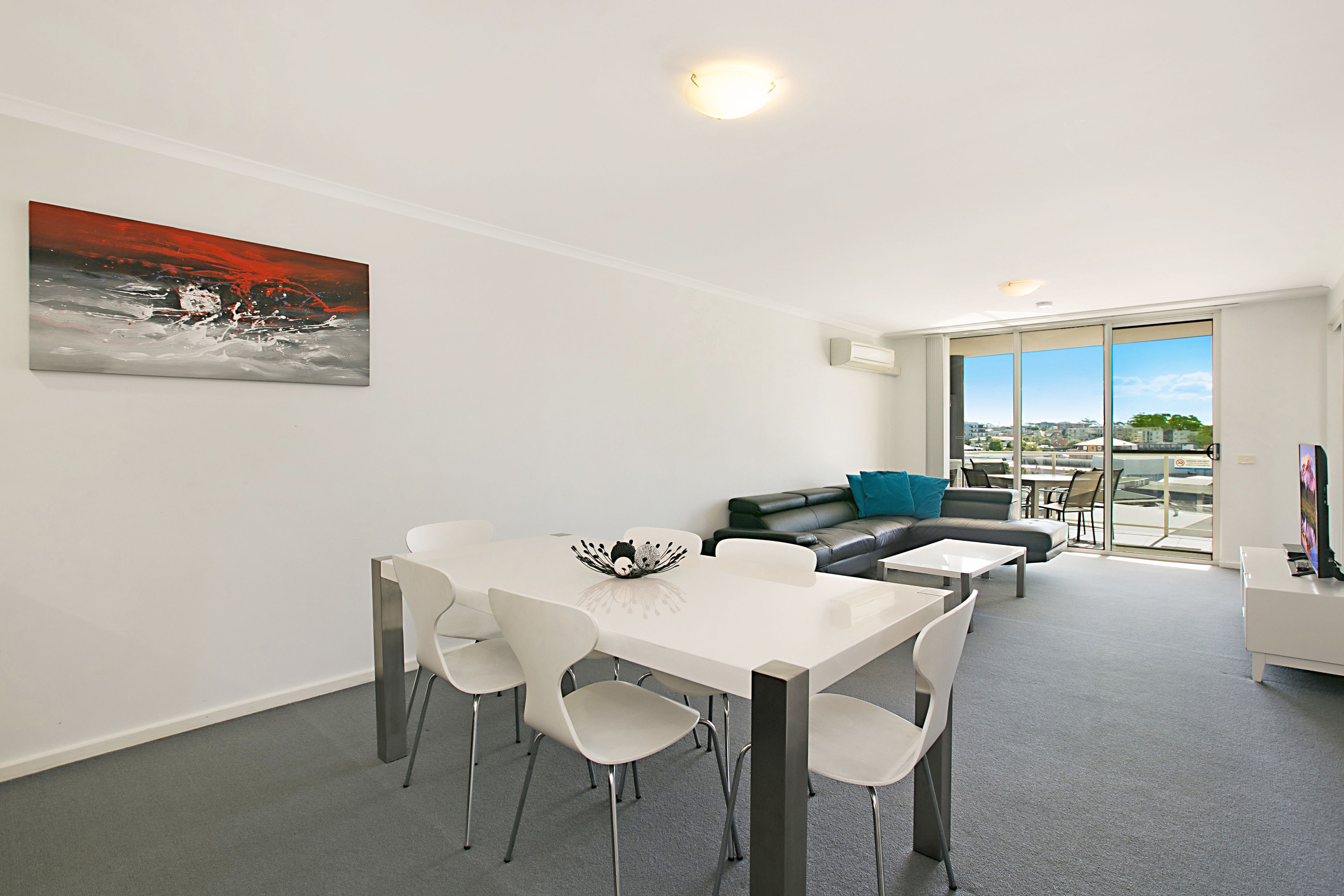 A modern living room with a dining area, a sofa, and a large window offering a city view.