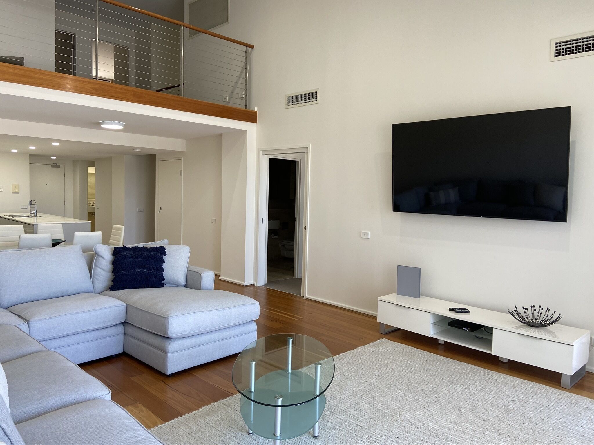 A modern living room with a sectional sofa, a glass coffee table, a flat-screen TV, and a white entertainment unit.