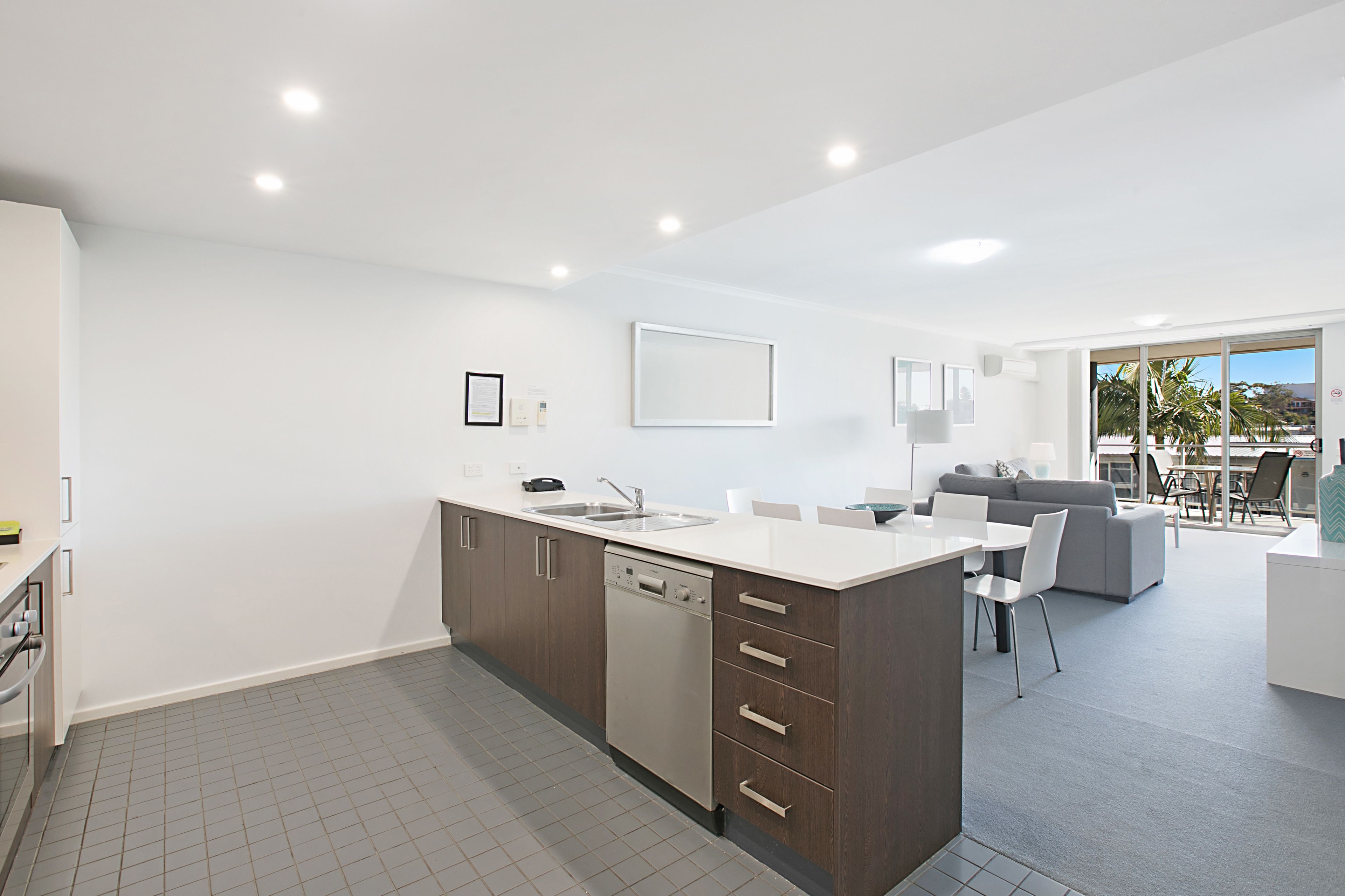 A modern kitchen with a dishwasher, a large island with a sink, and a dining area with a gray sofa and white chairs.